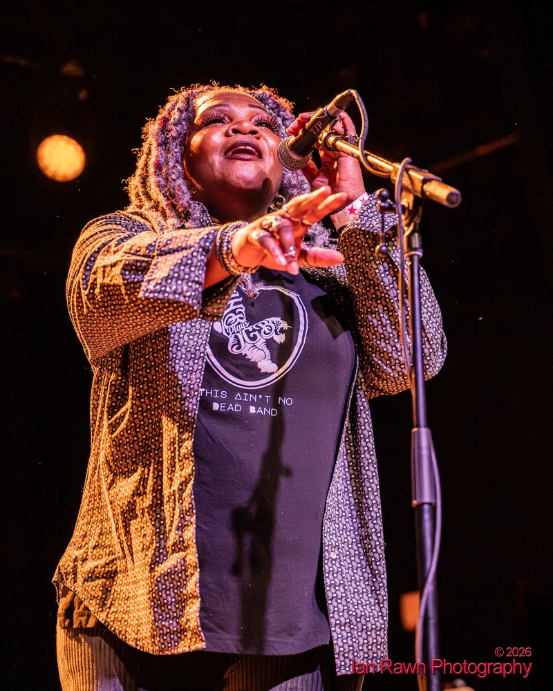 Trina Meade reaching out from the microphone mid-song under warm stage light