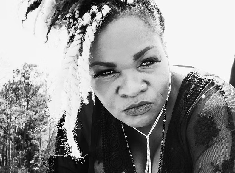 Black-and-white portrait of Trina Meade outdoors, locs falling across her shoulder